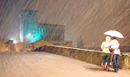 due persone con cane sul ponte del bisenzio mentre nevica. La Rocca sullo sfondo